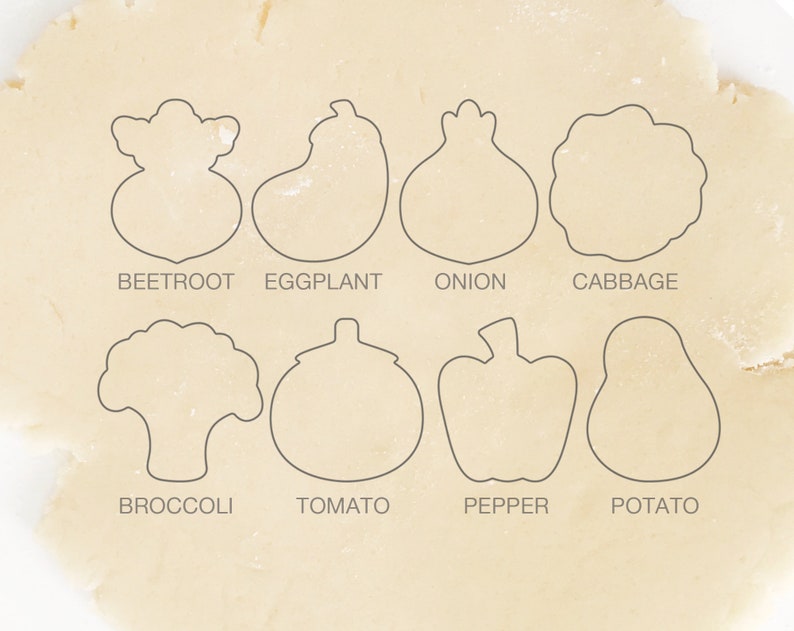 May include: A set of eight cookie cutters shaped like different vegetables, including a beet, eggplant, onion, cabbage, broccoli, tomato, pepper, and potato. The cutters are arranged on a white surface.