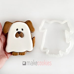 Op de afbeelding: Een bruine en witte spookhond koekjesvormpje met een witte spookhond koekje. De koekjesvormpje is gemaakt van plastic en het koekje is versierd met bruine glazuur.