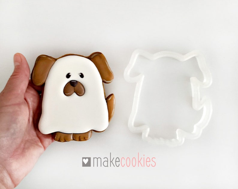 Op de afbeelding: Een bruine en witte spookhond koekjesvormpje met een witte spookhond koekje. De koekjesvormpje is gemaakt van plastic en het koekje is versierd met bruine glazuur.