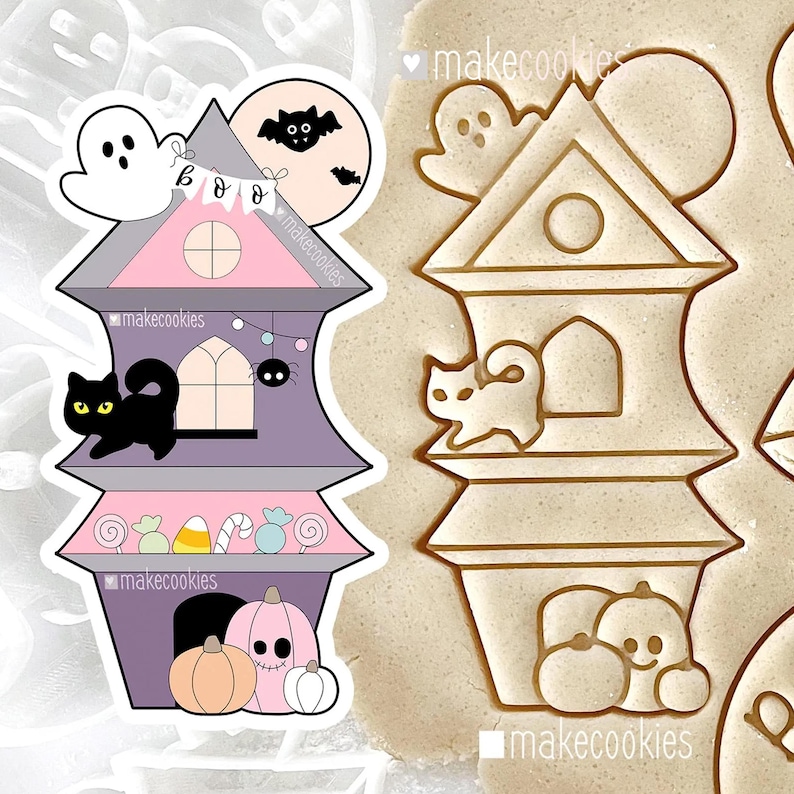 May include: A Halloween-themed cookie cutter in the shape of a haunted house. The house is purple, pink, and gray, with a black cat, ghost, and bat. The text "makecookies" is visible. The cookie cutter is next to a cookie with the same design.