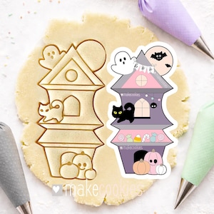 May include: Two Halloween-themed cookie cutters. One is a house-shaped cutter with a ghost, cat, and pumpkins. The other is a decorated house with a ghost, bat, and pumpkins. The cutters are on a sheet of dough.