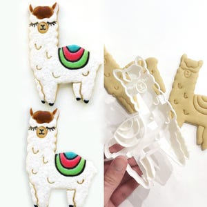 May include: Two llama-shaped cookies with white frosting, brown ears, and colorful saddle blankets. The cookies have black eyes and feet. A clear plastic llama cookie cutter is also shown, along with a baked cookie.