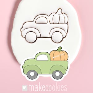 May include: A green pickup truck cookie cutter with a pumpkin in the bed. The cutter is shown in two forms: a white plastic cutter and a green and orange finished cookie. The text "makecookies" is at the bottom.