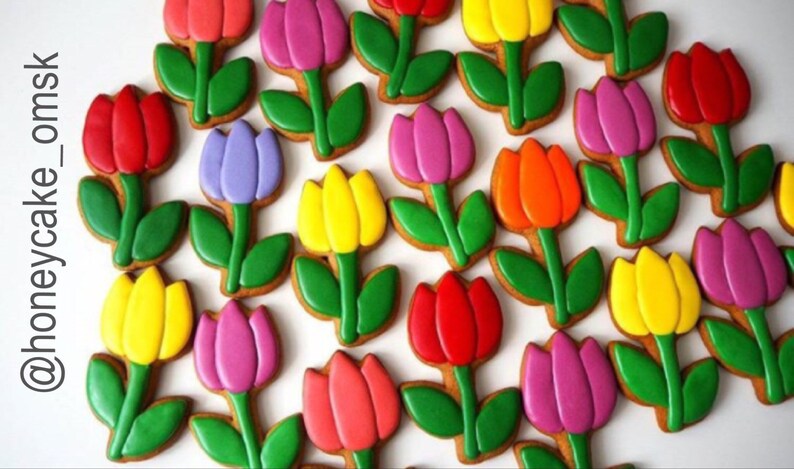 Op de afbeelding: Een verzameling kleurrijke gingerbreadkoekjes in de vorm van tulpen. De koekjes zijn versierd met glazuur in tinten rood, oranje, geel, groen, paars en roze.