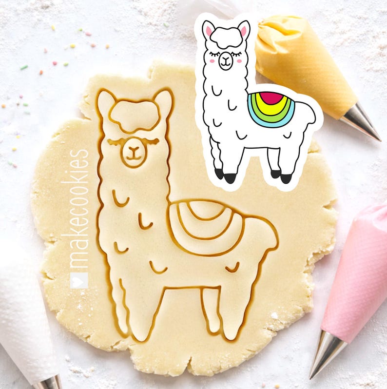 May include: A llama-shaped cookie cutter and a cookie cut-out on a light-colored surface. The cookie cutter is pressed into the dough, creating an imprint. A separate llama sticker with a rainbow blanket is also present. Two pastry bags are in the background.