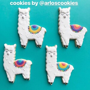 May include: Four llama-shaped cookies with white frosting and colorful saddle blankets. Each cookie has closed eyes and black feet. The cookies are decorated with rainbow-colored details and sit on a turquoise background. The text "cookies by @arloscookies" is at the top.