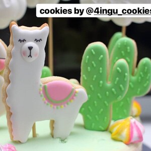 May include: Cookies decorated with white icing in the shape of a llama and green cactus. The llama cookie has a pink saddle and the cactus cookies have green icing with small green sprinkles. The text "cookies by @4ingu_cookies" is at the top.