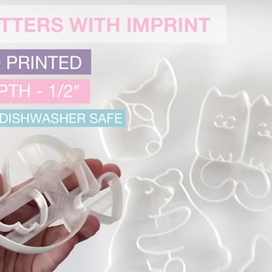 May include: A collection of clear 3D-printed cookie cutters in various shapes, including a gnome, two cats, and a bear. The cutters have a depth of 1/2 inch and are labeled "CUTTERS WITH IMPRINT" and "NOT DISHWASHER SAFE."