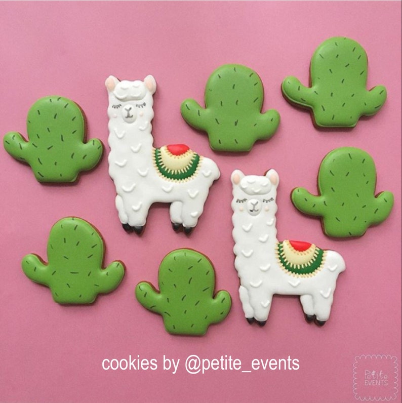 May include: Cookies decorated as white llamas with colorful saddle blankets and green cacti on a pink background. The cookies are arranged in a visually appealing pattern. The text "cookies by @petite_events" is at the bottom.