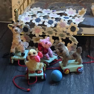Pode incluir: Uma coleção de animais de brinquedo em miniatura sobre rodas, incluindo uma girafa, um pato, um porco e um cão. Cada brinquedo é de uma cor diferente e tem uma corda vermelha presa. Uma bola azul está por perto. Os brinquedos estão em uma superfície de madeira.