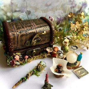 Puede incluir: Una escena de fantasía en miniatura con un cofre del tesoro marrón, una varita mágica, setas, una bola de cristal y botellas de pociones. La escena está sobre una superficie blanca con un fondo floral borroso. El cofre mide unos 5 cm de ancho.