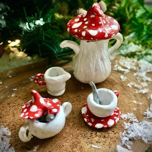 Könnte beinhalten: Ein Miniatur-Tee-Set mit einer Teekanne in Pilzform, Milchkännchen, Zuckerdose und Tasse mit Untertasse. Das Set ist weiß mit roten und weißen Punkten bemalt.