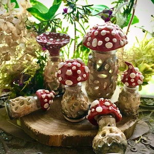 May include: A set of six ceramic mushroom bottle stoppers with red and white painted caps. The stoppers are in various sizes and have a rustic, hand-painted look.