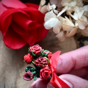 Peut inclure: Un petit bouquet de roses rouges avec des feuilles vertes et un nœud en ruban rouge.