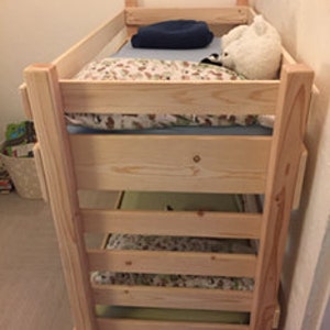 May include: A wooden bunk bed with three levels. The top level has a blue blanket and a white stuffed animal. The middle level has a patterned sheet and the bottom level has a patterned sheet.