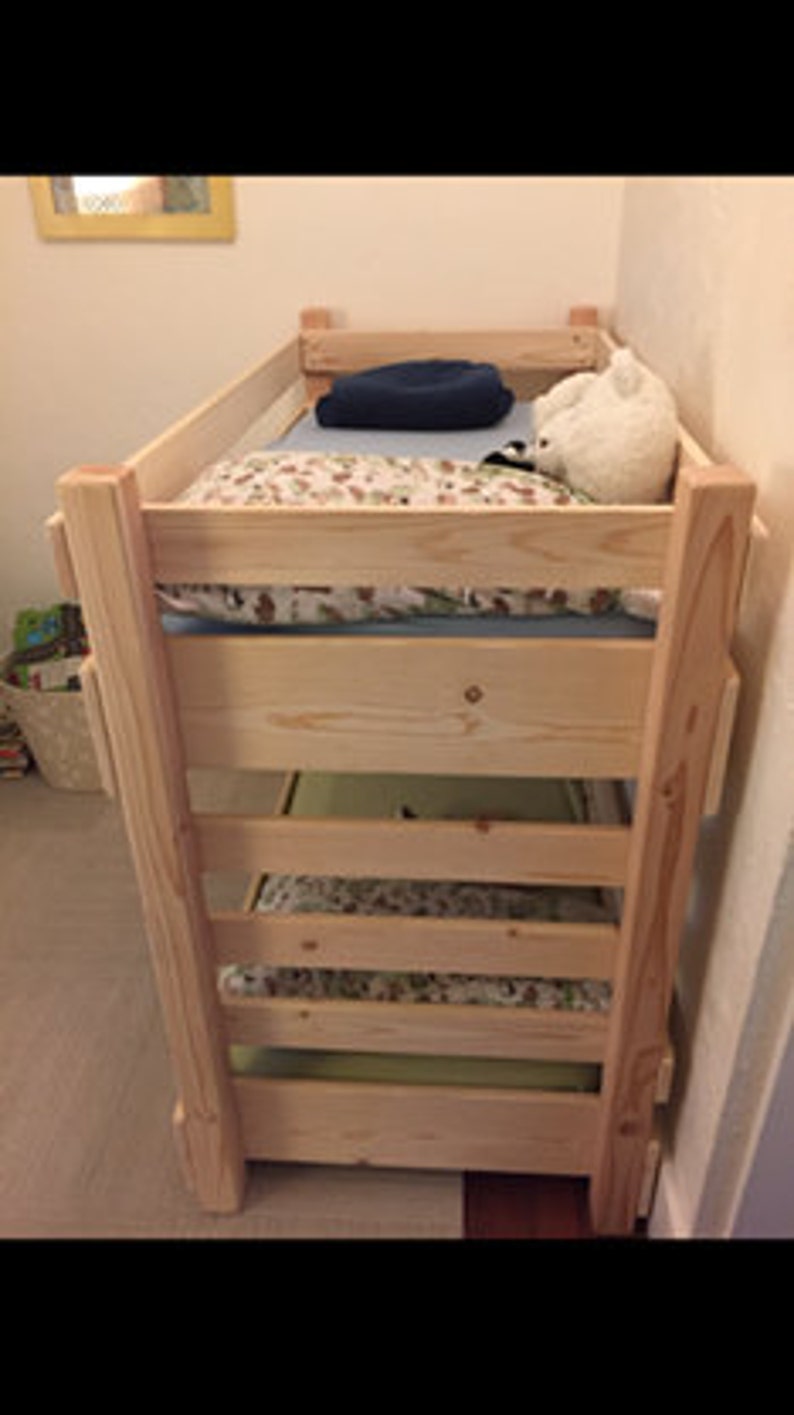 May include: A wooden bunk bed with three levels. The top level has a blue blanket and a white stuffed animal. The middle level has a patterned sheet and the bottom level has a patterned sheet.