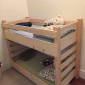 Puede incluir: Una litera de madera con dos colchones y un peluche en la litera superior.