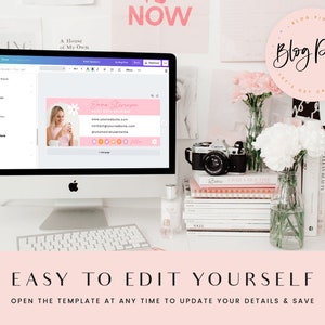 May include: A pink and white digital business card template with the text "Emma Stereagen" and "Blog Pixie" on a computer screen. The screen is on a white desk with a camera, flowers, and books.