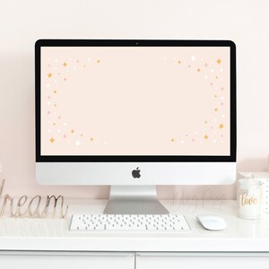 May include: A white desktop computer with a pink and gold star pattern on the screen. The computer is on a white desk with a gold metal word "dream", a white keyboard, and a white mouse. There is a pink and gold candle that says "love" on the desk.