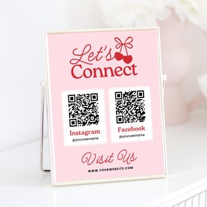 May include: Pink sign with the text "Let's Connect" in red cursive with two red cherries and a bow.  Two QR codes are below the text, labeled "Instagram" and "Facebook" with the text "@yourusername" below each.  The text "Visit Us" is below the QR codes in red cursive with the text "www.yourwebsite.com" below it.