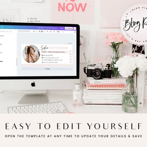 May include: A computer screen showing a pink and white business card template with a woman's photo and the text "Sophie SMITHSON" and "OWNER, Sophie Smithson Studio". The screen is on a white desk with a camera, flowers, and books.