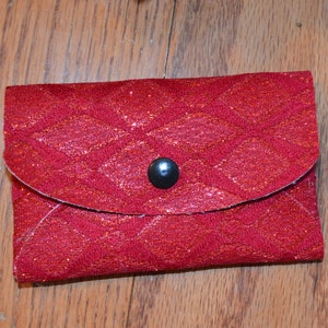 Puede incluir: Una cartera de tela roja acolchada con cierre de botón negro.