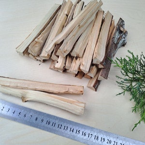 Puede incluir: Una pila de finos palitos de madera de color marrón claro, algunos de los cuales están apilados uno encima del otro. Una regla se coloca sobre la mesa junto a los palitos, con los números del 1 al 22 visibles. Una pequeña rama de follaje verde se encuentra a la derecha de los palitos.