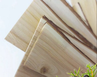 Könnte beinhalten: Stapel aus hellbraunen Holzbrettern mit einem Zweig Wacholderbeeren mit dunkelblauen Beeren und grünen Blättern.