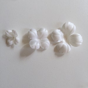 Puede incluir: Tres pétalos de flores de tela blanca, cada uno de un tamaño diferente. Los pétalos están dispuestos en una fila del más pequeño al más grande.