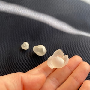 Peut inclure: Trois embellissements floraux en tissu blanc, deux petits et un grand, avec une surface délicate et texturée.