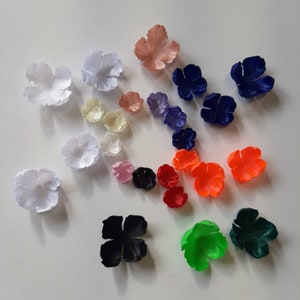 Puede incluir: Surtido de pétalos de flores de tela en varios colores, incluyendo blanco, rosa, rojo, naranja, verde, azul y negro. Los pétalos están dispuestos en un patrón circular sobre una superficie blanca.