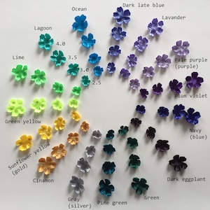 Puede incluir: Una carta de colores de 16 colores diferentes de flores de tela. Los colores están dispuestos en un círculo, con los colores más oscuros en la parte superior y los colores más claros en la parte inferior. Los colores son: azul oscuro, océano, lavanda, morado pálido (morado), violeta ciruela, azul marino (azul), berenjena oscura, verde, verde pino, gris (plata), canela, amarillo girasol (oro), amarillo verde, lima, laguna.