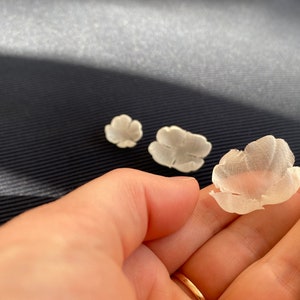 Könnte beinhalten: Drei weiße Stoffblumen, zwei sind geschlossen und eine ist offen, in einer Hand.