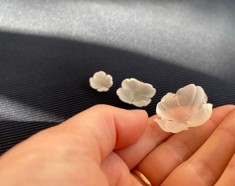 May include: Three white fabric flowers, two are closed and one is open, in a hand.
