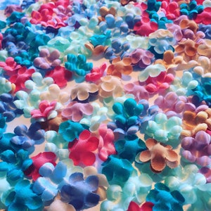 May include: A collection of small, fabric flower embellishments in various pastel colors, including pink, blue, purple, and teal.