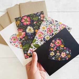 May include: Set of five greeting cards featuring floral designs. The cards are printed on white paper with a variety of floral patterns, including pink, purple, and yellow flowers. The cards are perfect for sending a special message to someone you care about.