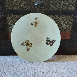 May include: A white round plate with three butterfly designs. The butterflies are brown, black, and white.