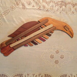 K&ouml;nnte beinhalten: Eine Holzskulptur eines Vogels, gefertigt aus verschiedenen Braunt&ouml;nen von Holz. Der Vogel ist in Flugposition dargestellt, mit ausgebreiteten Fl&uuml;geln.