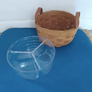 May include: A clear plastic divided serving bowl with three sections sits on a blue surface next to a brown wicker basket with leather handles.