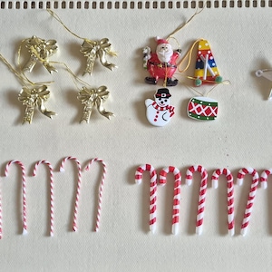 May include: A collection of Christmas ornaments, including gold bows, candy canes, star-shaped decorations, and miniature figures of Santa Claus and a snowman. The ornaments are in various colors, including red, green, and gold.