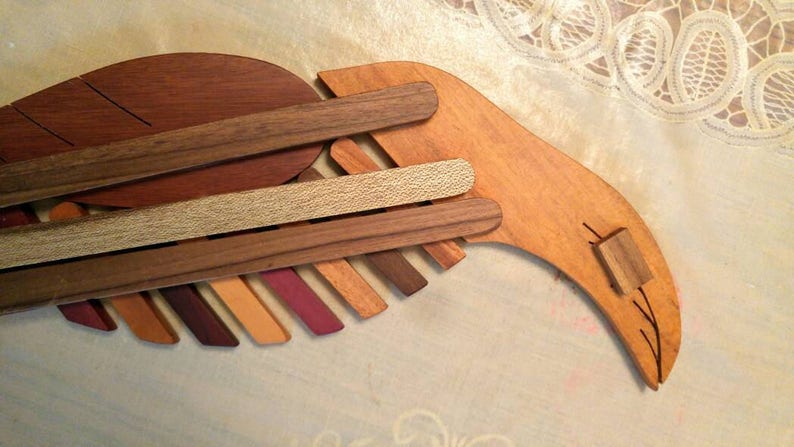 K&ouml;nnte beinhalten: Eine Holzskulptur eines Vogels, hergestellt aus verschiedenen Holzarten, mit einer nat&uuml;rlichen Holzveredelung. Der Vogel hat einen langen, gebogenen Schnabel und einen Fl&uuml;gel aus &uuml;bereinanderliegenden Holzst&uuml;cken.