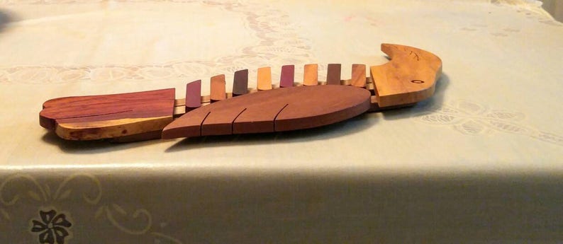 K&ouml;nnte beinhalten: Eine Holzskulptur eines Vogels mit einem segmentierten K&ouml;rper, der in Braun-, Rot- und Lilat&ouml;nen bemalt ist. Der Vogel hat einen langen, spitzen Schnabel und einen abgerundeten Schwanz.