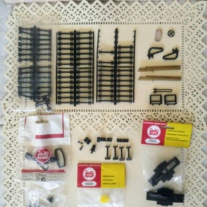 May include: A set of black plastic model train track pieces, including straight track, curved track, and a stop block. The pieces are packaged in clear plastic bags with labels that say "Lehman Cross Bahn" and "1052" and "5025".
