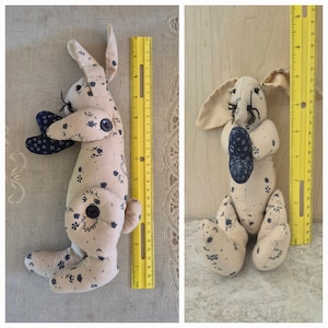 May include: Two handmade fabric bunny rabbits with black floral patterns. The bunny on the left is holding a heart-shaped fabric piece. The bunny on the right is sitting with its paws together. Both bunnies are approximately 10 inches tall.