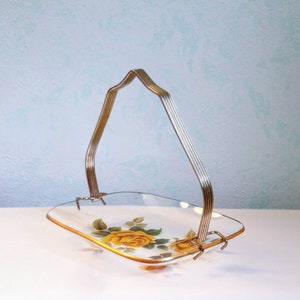 May include: A glass serving tray with a gold rim and a floral design featuring yellow roses. The tray has a metal handle.