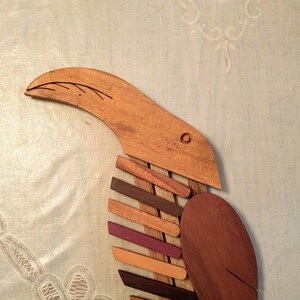 K&ouml;nnte beinhalten: Eine Holzskulptur eines Vogels mit einem langen Schnabel und einem K&ouml;rper aus mehreren Holzst&uuml;cken in verschiedenen Braunt&ouml;nen, Orange und Lila.