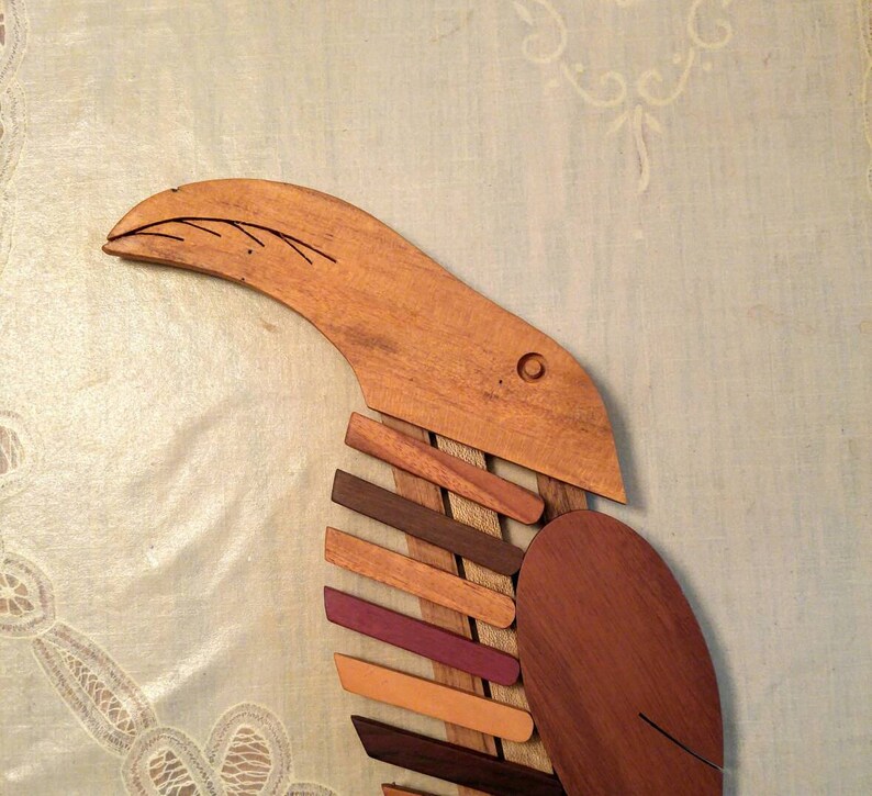 K&ouml;nnte beinhalten: Eine Holzskulptur eines Vogels mit einem langen Schnabel und einem K&ouml;rper aus mehreren Holzst&uuml;cken in verschiedenen Braunt&ouml;nen, Orange und Lila.