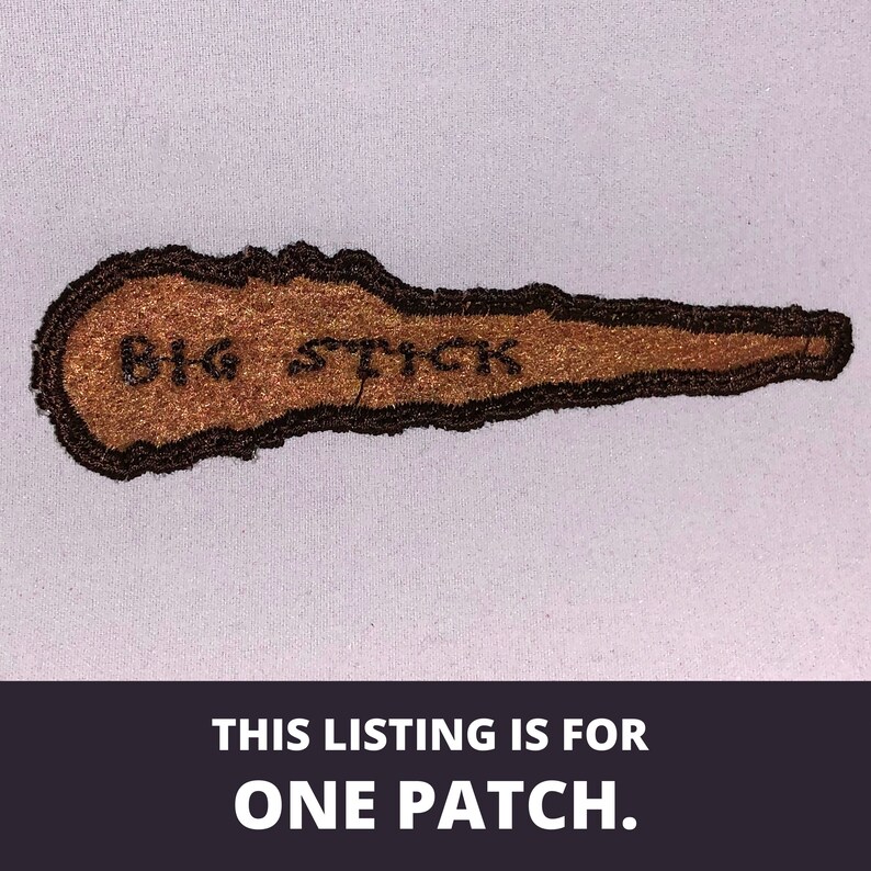 May include: Brown embroidered patch with black stitching. The patch is shaped like a long, thin stick with the words "BIG STICK" embroidered on it.