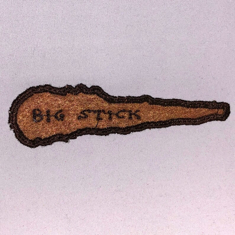 May include: Brown embroidered patch with the text "BIG STICK" in black thread.