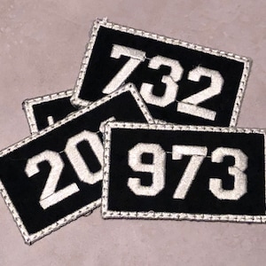 May include: Four black fabric patches with white numbers. The numbers are 732, 20, 973, and another number that is partially obscured.